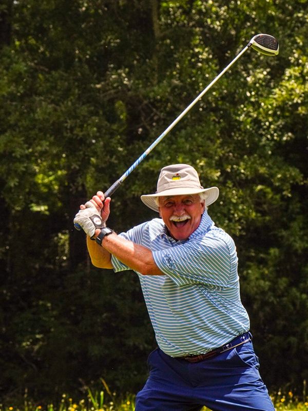 Smiling elderly man playing golf in sunny weather.
