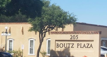 Sign for Boutz Plaza at 205, with a tree and building in the background.