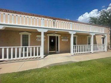 Historic adobe building with white columns and porch under a blue sky.