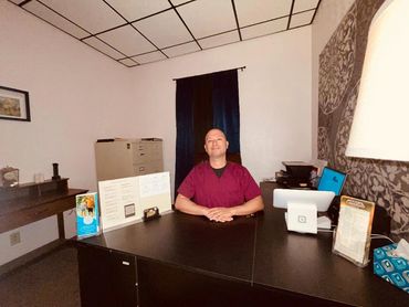 Man sitting at a desk in a small office with paperwork and a computer.