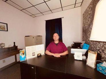 Man sitting at a desk in a small office with paperwork and a computer.