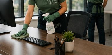 Two professional cleaners tidying an office desk and window.