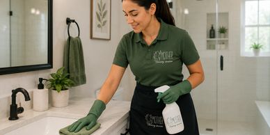 A woman in green uniform cleaning a bathroom countertop.