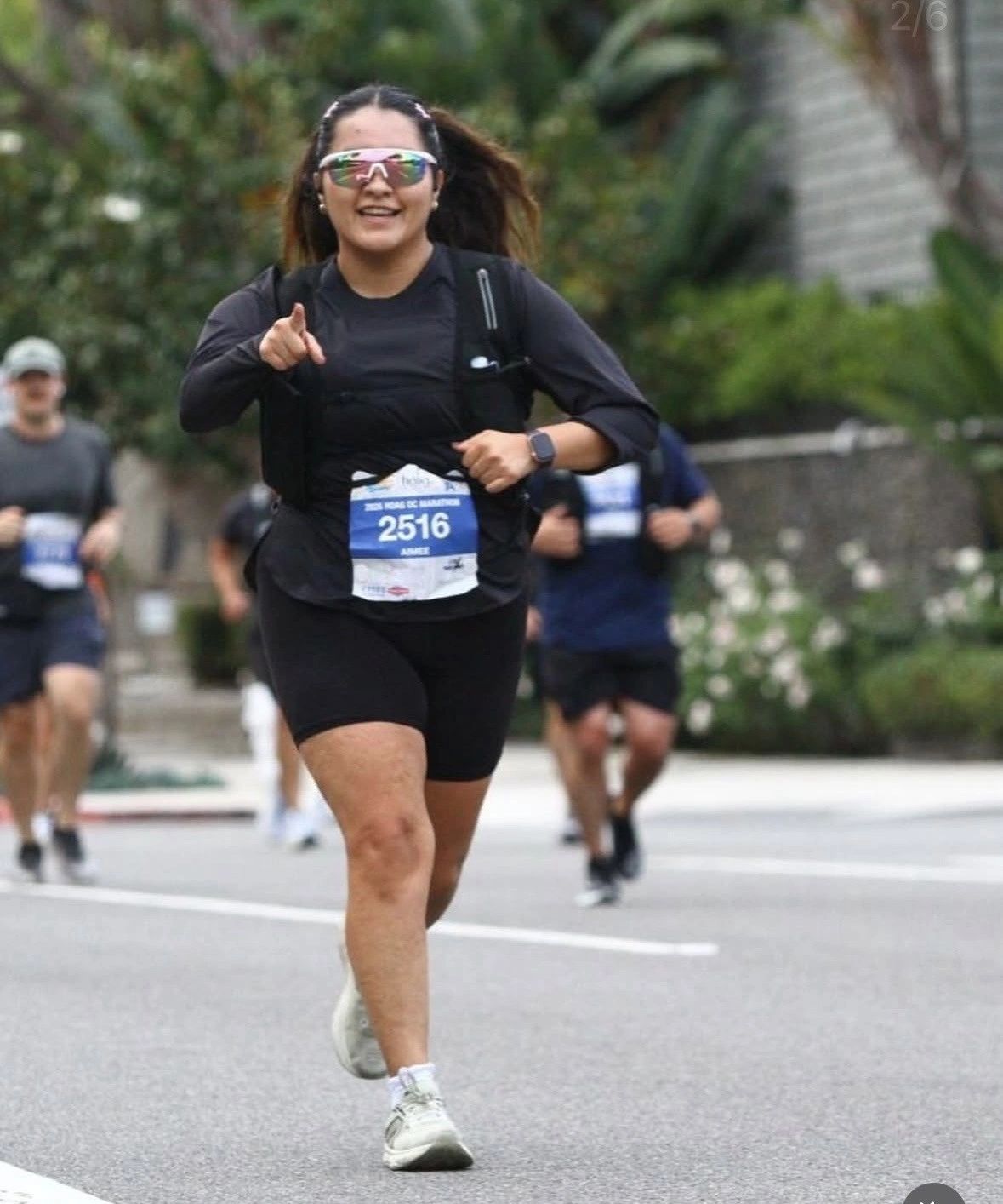 A smiling runner wearing sunglasses points forward during a marathon race.