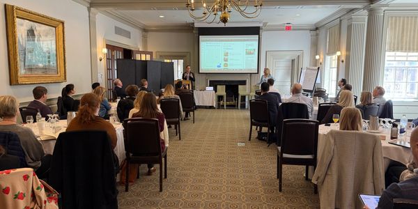Attendees seated around tables during a presentation at the Harvard Faculty Club