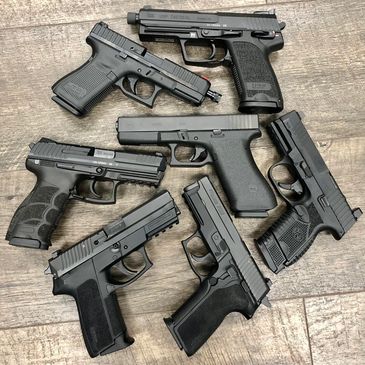 Collection of modern pistols displayed in a circle pattern. Glock, Sig Sauer and HK.