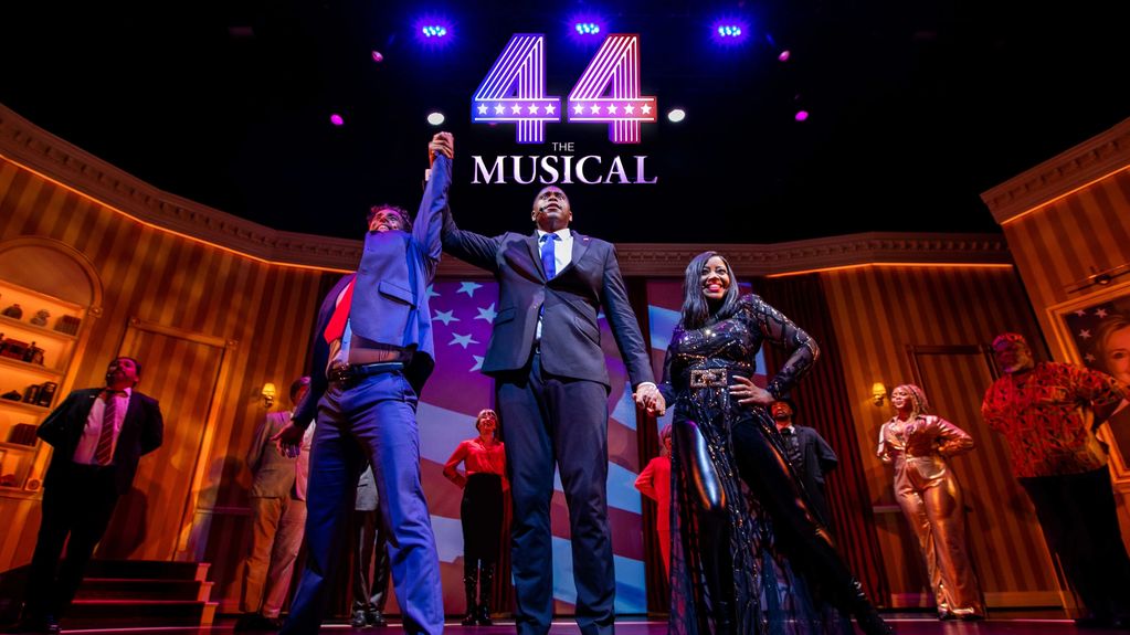 Cast of "The 44 Musical" takes a bow on stage with patriotic backdrop and vibrant lighting.