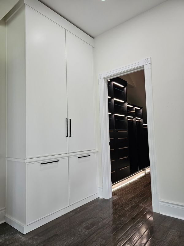 White cabinet with black handles next to a doorway showing illuminated black shelves inside.