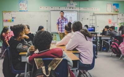 Classroom full of students sitting in desks and listening to the male teacher.