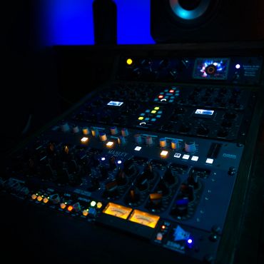 Audio mixing equipment with glowing lights in dark room.
