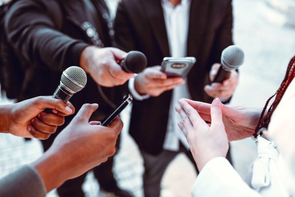 A close-up image of a press interview scene, showing multiple microphones