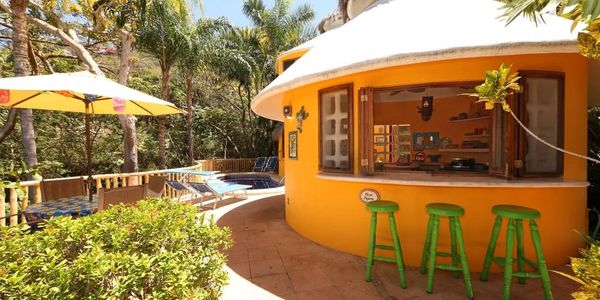 Tropical outdoor bar with green stools and yellow umbrella in sunny garden.