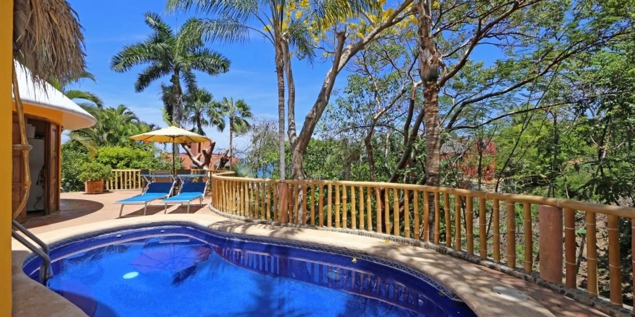 Tropical poolside with blue water, lounge chairs, and lush greenery under a clear sky.