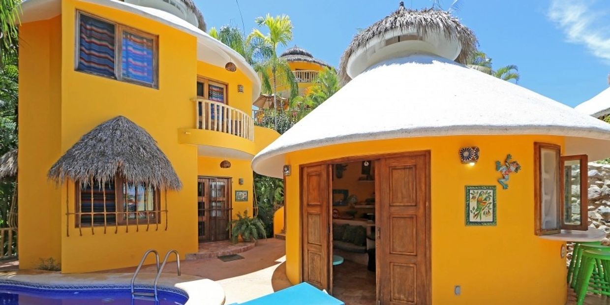 Colorful yellow houses with thatched roofs and a small pool in a sunny tropical setting.