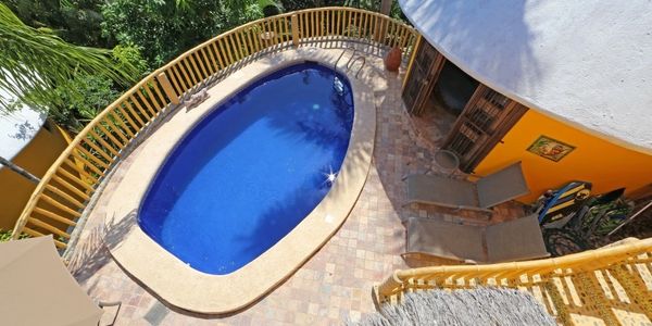 View of a small, oval pool surrounded by a tiled patio and yellow railing.