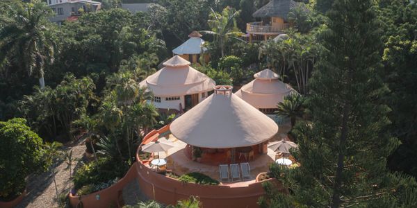 Round, thatched-roof huts surrounded by lush greenery in a tropical setting.