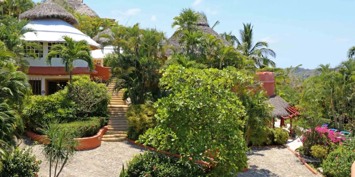 Tropical resort with lush greenery and thatched-roof buildings.