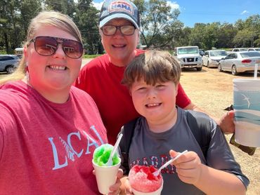Family enjoying colorful shaved ice treats on a sunny day outdoors.