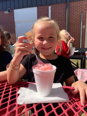 Smiling girl enjoying a pink shaved ice on a sunny day outdoors.