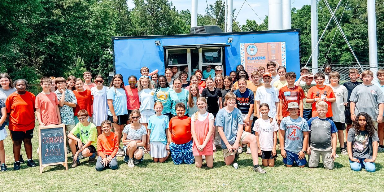 A large group of children posing outdoors with a 'Congrats Class of 2031' sign.