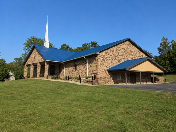 Brick church building with blue roof and white steeple under clear sky.