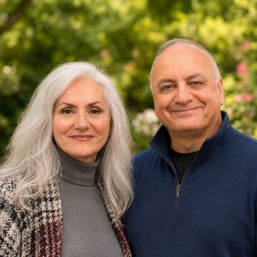 Smiling mature couple posing outdoors with greenery in the background.