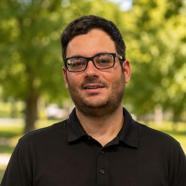 Man wearing glasses and a black polo shirt outdoors.