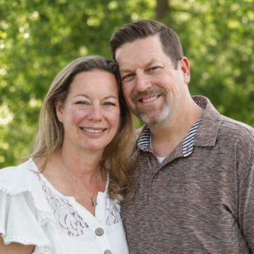Smiling couple posing outdoors with greenery background.