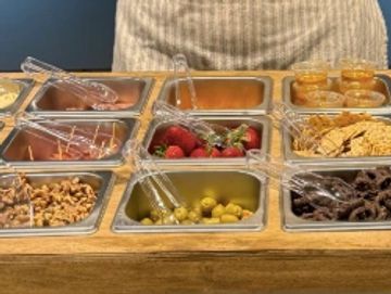 Woman in apron stands behind a table with various food items.