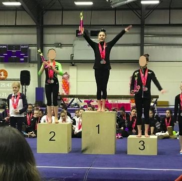 Young gymnasts on winners' podium holding trophies.