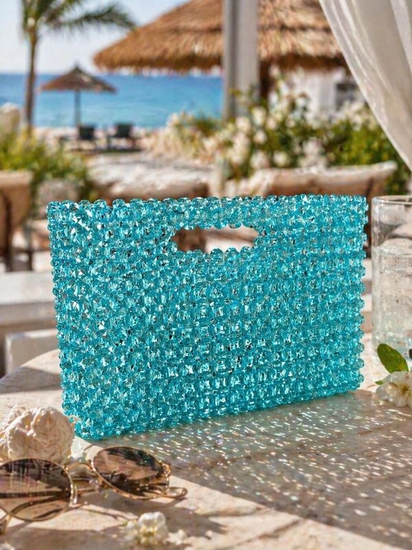 A sparkling blue beaded handbag sits on a sunlit table by the beach.
