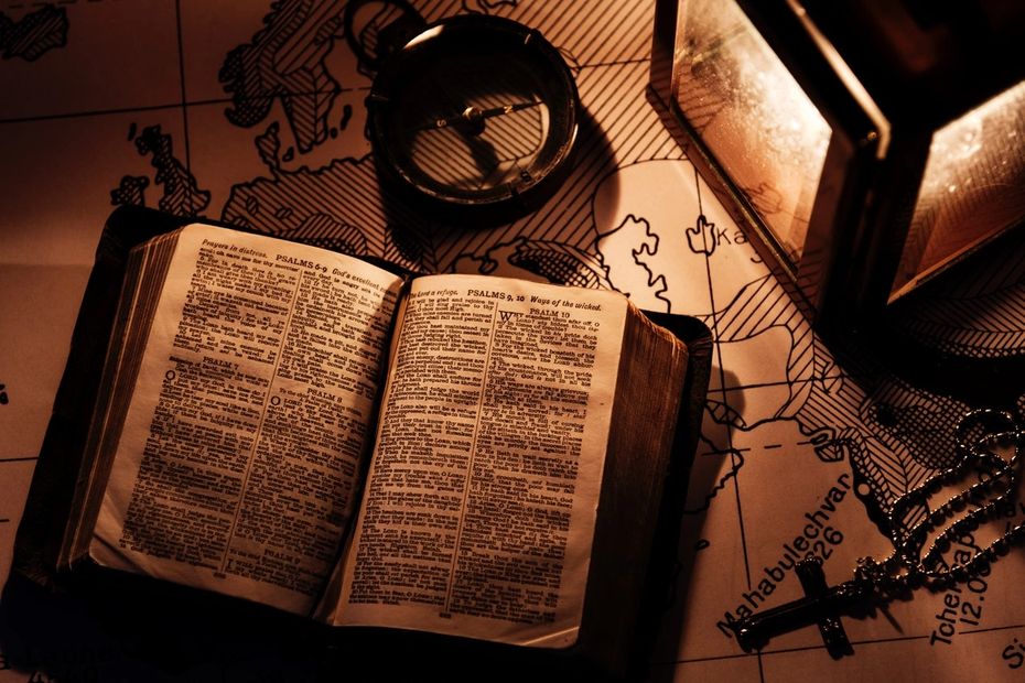 Open Bible, compass, and cross necklace on a map.
