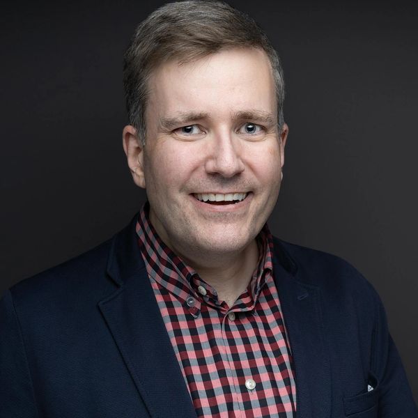 Smiling man in checkered shirt and blazer.