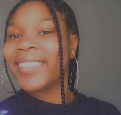 Smiling young woman with braided hair and hoop earrings.