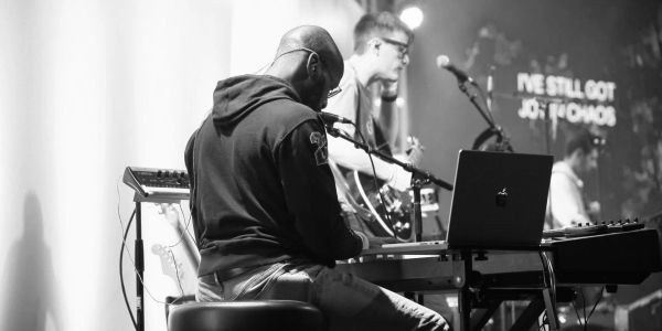 Musicians performing on stage with keyboards and guitars.