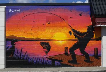 Mural of a fisherman catching a fish at sunset by a lake.
