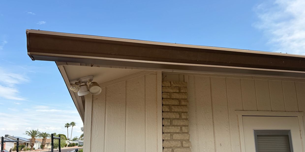 Corner of a beige house with outdoor lights and a clear sky.