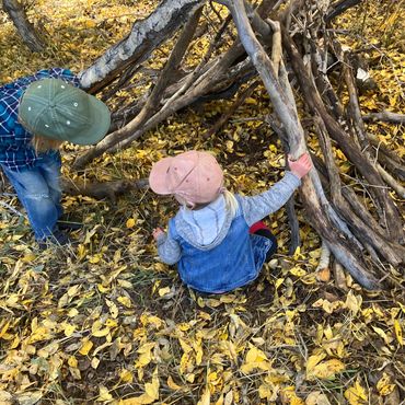 Two children building a shelter with branches in a leafy forest.