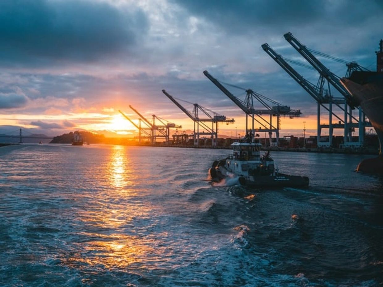 Photo of container port at sunset with small boat sailing towards the port.