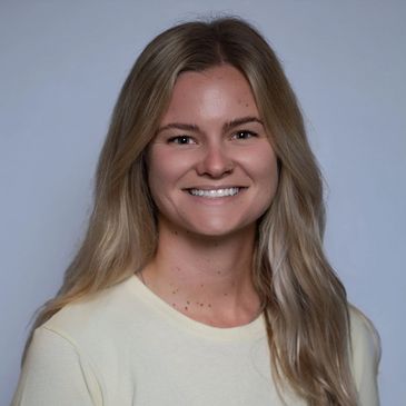 Smiling young woman with long blonde hair wearing a light yellow shirt.