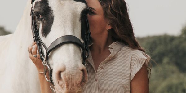 A woman gently embraces a white horse with black markings on its face.