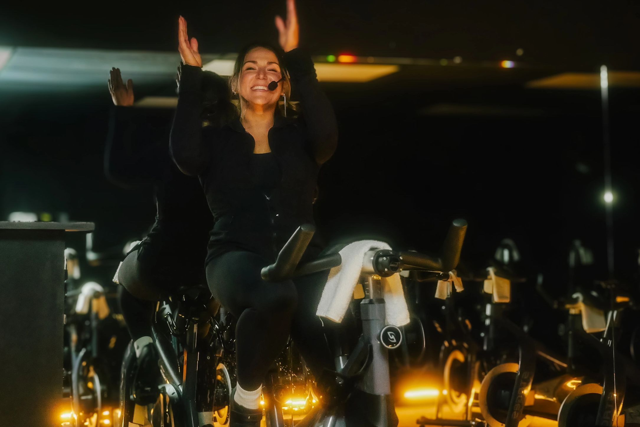 Joyful instructor leading a spin class in a dimly lit room.
