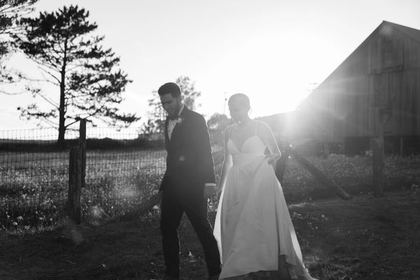 Black and white photo of a couple walking hand in hand outdoors at sunset.