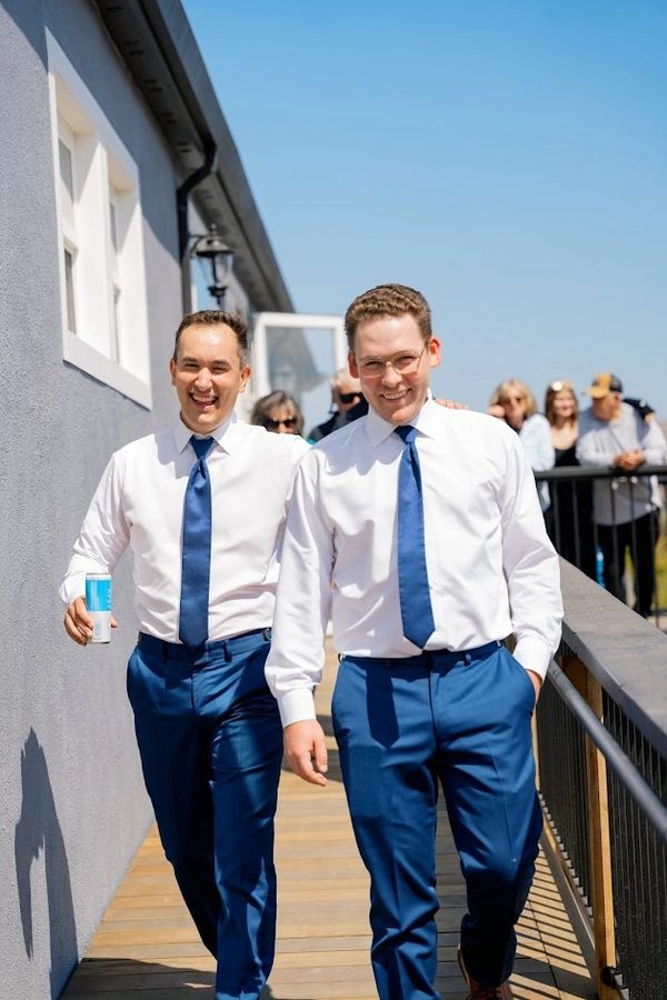 Two men in white shirts and blue ties walking outside on a sunny day.