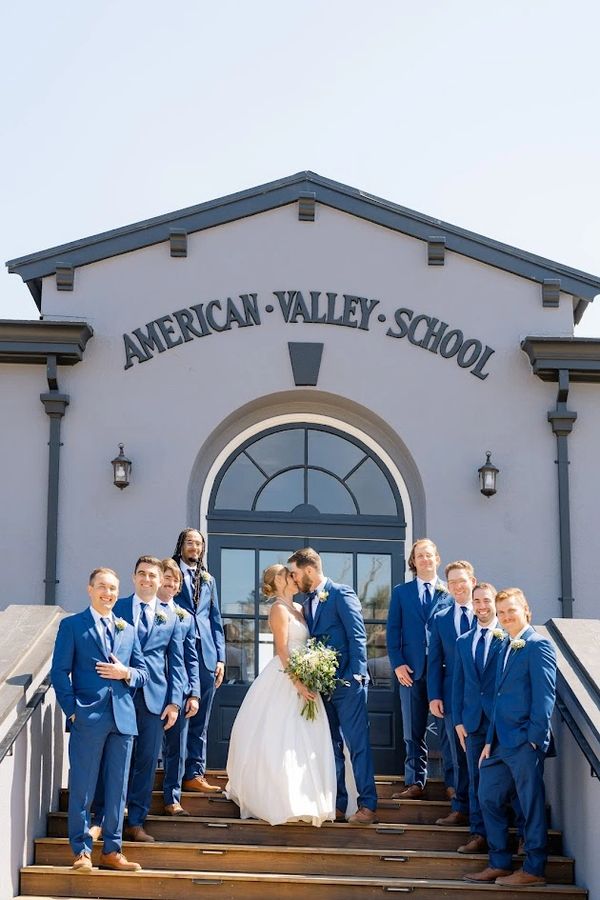 Bride and groom kiss on school steps with groomsmen in blue suits.