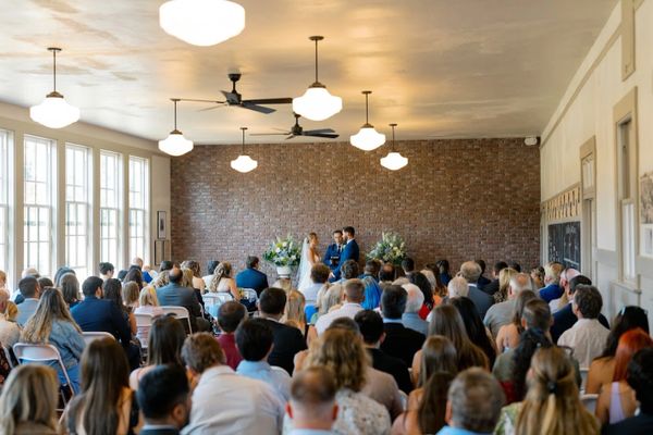 Indoor wedding ceremony with couple and guests facing a brick wall.