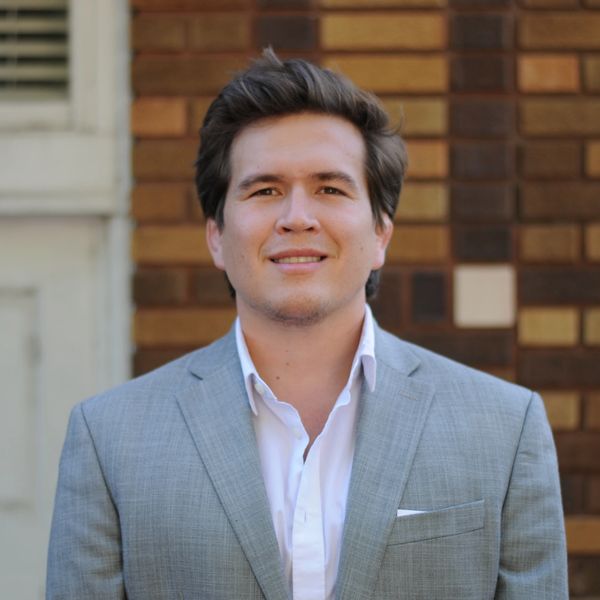 A man in a suit smiling in front of a brick wall.