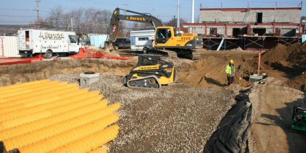 Construction site with heavy machinery and large yellow pipes.