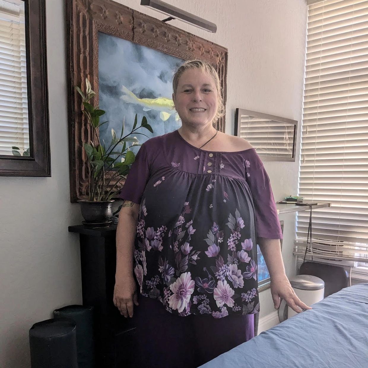 Woman smiling indoors with a floral purple top.
