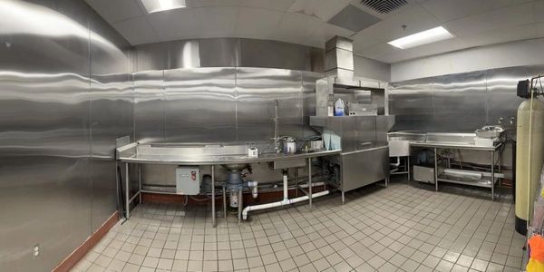 A clean, industrial stainless steel kitchen with tiled floors.